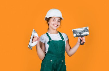 Çalışmaya hazırım. Mutlu kız spatula aleti kullanır. Genç müteahhit güvenlik kaskı takıyor. Koruyucu şapkalı genç işçi. Kendine güvenen çocuk spatulayı tamir ederken kullanır. İnşa ve yenileme konsepti.