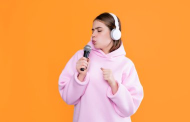 Sarı arka planda mikrofonu olan kulaklıklı komik bir genç kız..