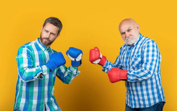 image of generation men fighting wear boxing gloves. two generation men fighting isolated on yellow. generation men fighting in studio. generation men fighting on background.