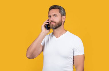 thoughtful man talk on smartphone in studio. man talk on communication smartphone. man has smartphone communication talk. concept of communication. man talk on smartphone isolated on yellow.