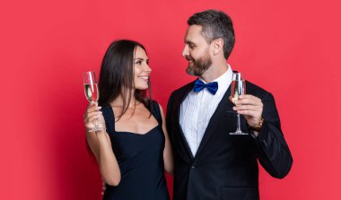 happy couple cheering and celebrate on background. photo of couple cheering and celebrate with champagne. couple cheering and celebrate isolated on red. couple cheering and celebrate in studio.