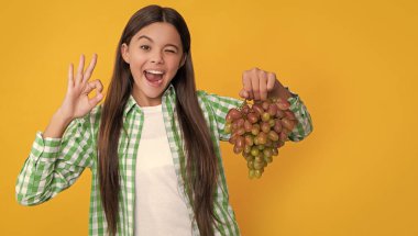 winking child with grapes bunch on yellow background. dieting.