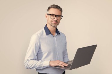 mature boss in eyeglasses working on computer on grey background.