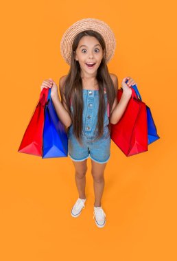 Sarı arka planda alışveriş torbaları olan afallamış genç bir çocuk..