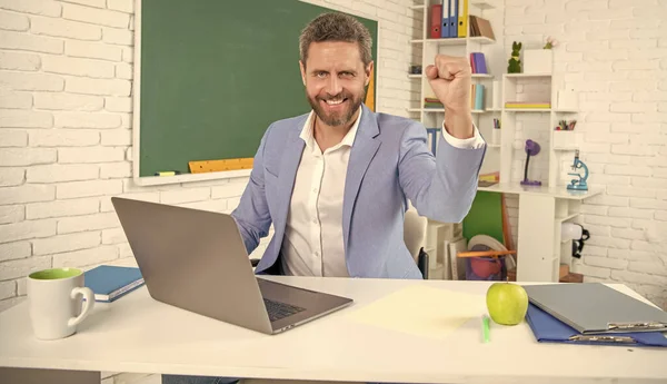 school teacher in classroom with computer at blackboard. success.