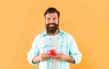 Ciddi sakallı adam sabah kahvesini sarı arka planda içer..