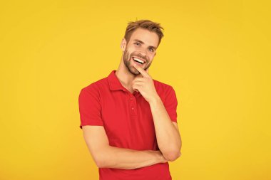 Sarı arka planda sakallı neşeli genç bir adam. Saç ve sakal bakımı. Kendine güvenen ve yakışıklı, tıraşsız adam. Erkek modası. Erkek güzelliği. Kırmızı gömlekli bir adamın portresi..