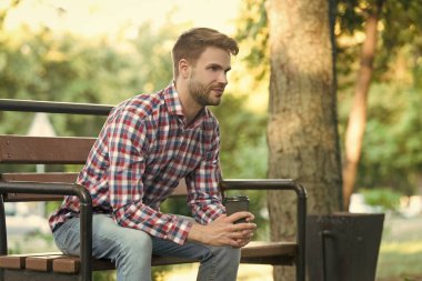 Parktaki bankta kahve fincanı olan kareli gömlekli genç adam..