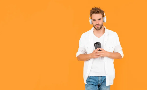 online education. back to school. young guy in headphones drink coffee. music lover. listen to music. wireless device accessory. new technology. man in modern earphones with coffee cup, copy space.