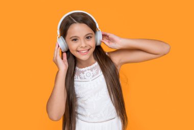 happy teen girl listening music in headphones on yellow background. clipart