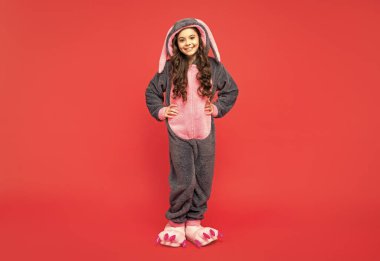 Kırmızı arka planda rahat ve rahat bir uyku elbisesi içinde mutlu bir çocuk..