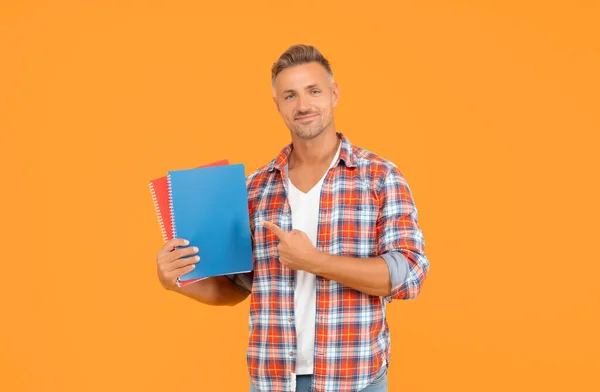 Happy man student pointing finger at copybooks yellow background, education.