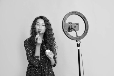 Uzun kıvırcık saçlı çocuk blogda pudra fırçası videosu çekiyor.