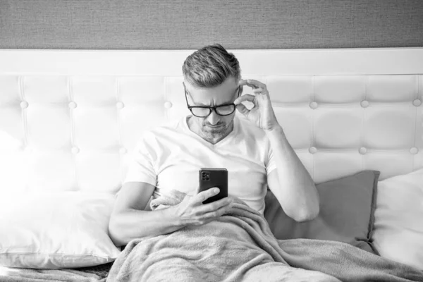 戴眼镜躺在床上看书电话的成熟男人 — 图库照片