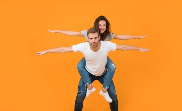 stock image Happy playful girl and guy pretend flying doing piggyback ride yellow background, couple.