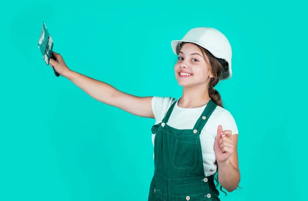 自信のある子供は修理中にへらを使う 建築と改修の概念です ハッピーガールはへらツールを使う ティーンビルダーは安全ヘルメットを着用します 若い労働者が保護ハード帽子をかぶって — ストック写真