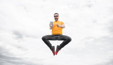 Şaşırmış bir adam zıplıyor ve gökyüzünde akıllı telefon sunuyor..