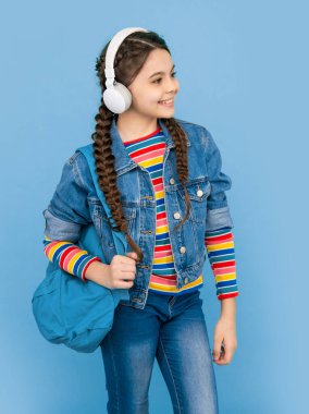 Kulaklıkla müzik dinleyen liseli kız. Genç kız okula geri döndü. Mutlu genç mavi arka plan. Resmi olmayan eğitim.