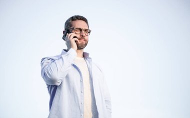 Gözlüklü adamın telefonda konuşması. Adam akıllı telefondan konuşuyor. Gökyüzü arka planında insan iletişimi. Boşluğu kopyala.