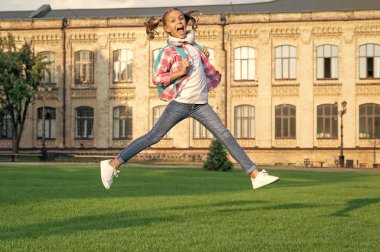 Happy teen girl jumping in school yard outdoors, back-to-school.