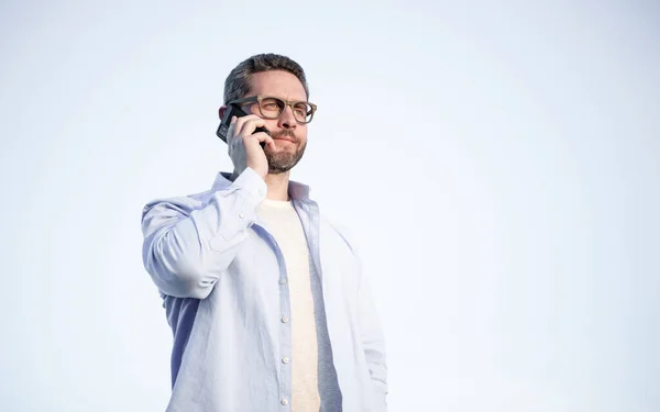 communication of man in glasses talk on phone. man talking on smartphone. man communication talk on sky background. copy space.