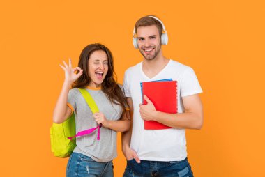 Modern eğitim. Bilgi günü. Erkekler ve kızlar defterlerini tutarlar. Üniversite öğrencileri sarı arka planda. Çalışma kitabıyla çalış. Tamam. Kulaklık ve sırt çantalı neşeli bir çift. Okula geri dön..