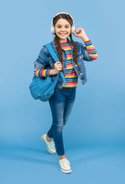 Kulaklıkla müzik dinleyen mutlu genç kız mavi arka plan, eğitim. Okul eğitimi. Resmi olmayan eğitim.