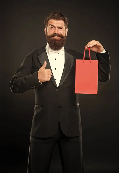 stock image glad man in tuxedo bow tie formalwear on black background with shopping bag. shopping sale. copy space. thumb up.