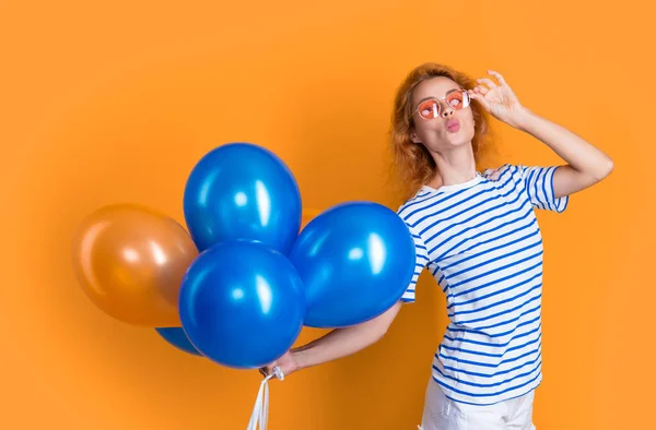 woman send kiss with birthday balloon in sunglasses. happy birthday woman hold party balloons in studio. woman with balloon for birthday party isolated on yellow background.