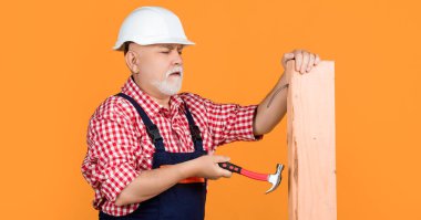 serious aged man woodworker in helmet on yellow background.