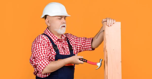 stock image serious aged man woodworker in helmet on yellow background.