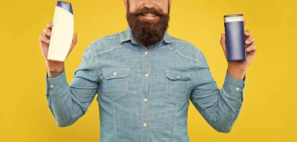 stock image cropped happy brutal bearded man choosing shampoo bottle on yellow background, presenting toiletries.