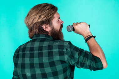 Melodiyi yakala. Olgun karizmatik erkek vokalist. Mikrofonda şarkı söyleyen sakallı adam. Sahnede özgüven ve karizma. Kareli gömlek giyen sakallı bir adam. Rock müzik. Erkek karaoke şarkıcısı.