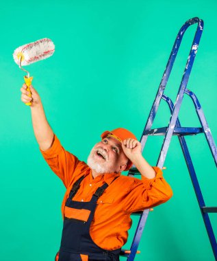Kıdemli boyacı merdivende paten kullanır. Duvarı yeşile boyamak. İş kıyafetleri içinde profesyonel bir ressam. Odada duvar boyama işçisi. Tekerlekli erkek dekoratör.