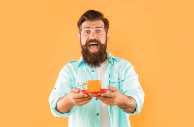 Şaşırmış sakallı adam sabah kahvesini sarı arka planda içer, kapuçino.