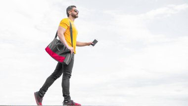 Guy tourist holding travel bag and document sky background, copy space.