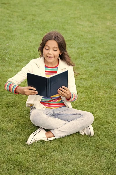 inspired teen girl read book sitting on grass. reading book. reader girl with book outdoor.