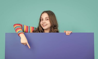 Gülümseyen çocuk reklam için fotokopi alanı olan boş mavi kağıdın arkasında.