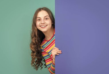glad girl behind blank blue paper with copy space for advertisement.