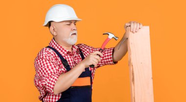 serious old man woodworker in helmet on yellow background.