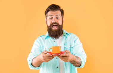 Sarı arka planda kahve ve kapuçino ile gömlekli, traşsız bir adam şaşırdı..