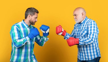 generation men fighting in studio, confrontation. generation men fighting on background. photo of generation men fighting wear boxing gloves. two generation men fighting isolated on yellow. clipart