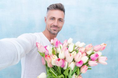 Sevgililer Günü laleli mutlu bir adamın fotoğrafı. Sevgililer günü laleleri olan bir adam. Stüdyoda sevgililer günü laleleri olan bir adam. Sevgililer günü laleleri olan bir adam mavi arka planda izole edilmiş..
