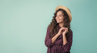 Mavi arka planda uzun sarı kıvırcık saçlı, hasır şapkalı pozitif çocuk..