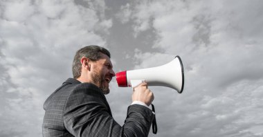 businessman shout in loud hailer on sky background.