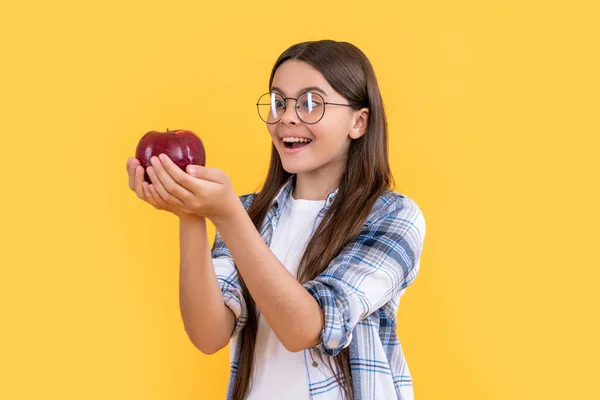 smiling teen girl with apple in studio. teen girl with apple on background. photo of teen girl with apple fruit. teen girl with apple isolated on yellow.