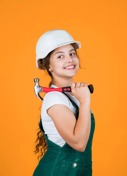 ready to work. building and repair tools. repairman. small girl repairing in workshop. cheerful kid in helmet hold hammer. carpentry and woodworking concept. teen child using hammer tool.