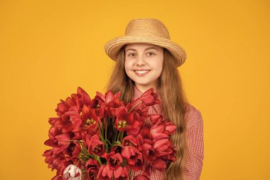 Sarı arka planda bahar lale çiçeklerini tutan şapkalı neşeli çocuk..