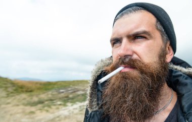 Dağda sigara içen bir adamın fotoğrafı, kopyalama alanı. Dışarıda sigara içen bir adam. Sigara içen sakallı bir adam. Sigara içen sakallı adam..