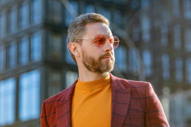 Havalı adam dışarıda güneş gözlüğü takıyor. Ceket giyen şık bir adamın fotoğrafı. Dışarıda ceketli şık bir adam var. Sokakta şık bir adam.